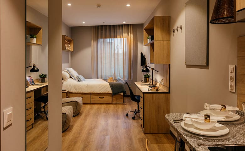 A comfy single room at student residence Livensa Living includes a bed, a desk, a kitchen and bathroom 