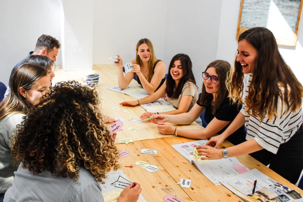 students sitting at a table laughing and playing a game to practice spanish